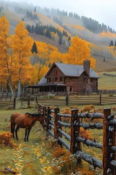 a brown horse standing next to a wooden fence in front of a log cabin on a hillside