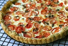 a pizza sitting on top of a cooling rack covered in cheese and toppings with tomatoes