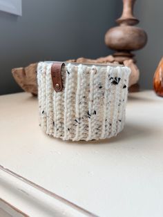 a white knitted cup holder sitting on top of a table next to a wooden object