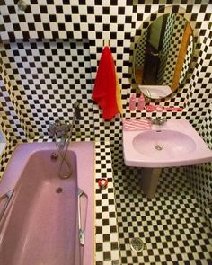 a bathroom with black and white checkered walls, pink bathtub, sink and mirror