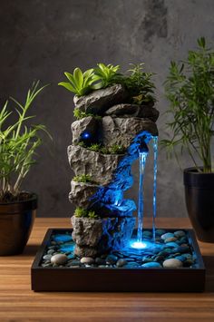 a water fountain is lit up with blue lights and surrounded by rocks, plants and stones