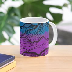 a purple and blue coffee mug sitting on top of a table next to a book