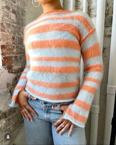 a woman standing in front of a brick wall wearing an orange and white striped sweater