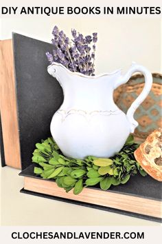 a white vase with lavenders in it sitting on top of a book and some bread