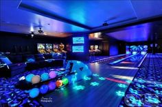 a bowling alley is lit up with blue lights and colorful balls on the floor in front of it