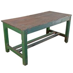 an old wooden table sitting on top of a white floor next to a green bench