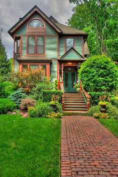 a green house with red trim and brick walkway leading to the front door is surrounded by lush greenery