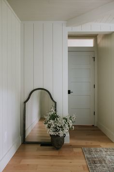 a vase with flowers sitting on top of a wooden floor next to a mirror and door