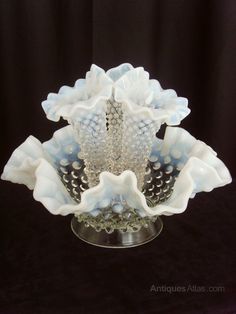 a glass vase sitting on top of a black table next to a black background with white flowers in it