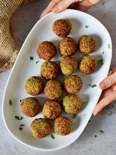 a white plate filled with meatballs on top of a table next to two hands