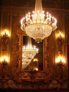 a chandelier hanging from the ceiling in front of a mirror with lights on it