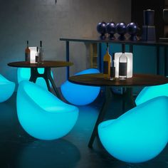 some chairs and tables are lit up with blue lights in the dark room, while bottles sit on top of them