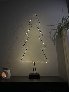 a lighted christmas tree sitting on top of a table next to a potted plant