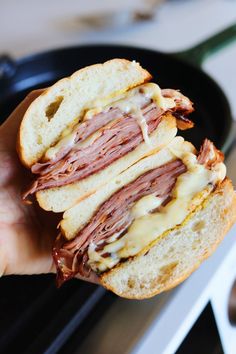 a hand holding a sandwich with meat and cheese