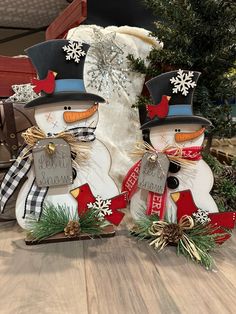 two snowmen standing next to each other on top of a wooden floor near a christmas tree