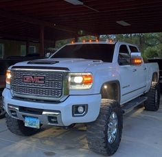 a large white truck parked in a garage next to another black truck with lights on