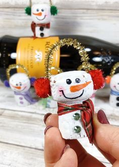 someone is holding a snowman ornament in front of some wine bottle holders