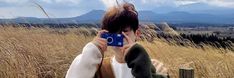 a person holding up a cell phone to their face in front of some tall grass