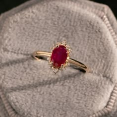 a red stone ring sitting on top of a white cloth covered cushioned surface,