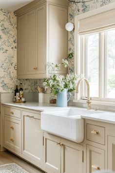 a white kitchen sink sitting under a window next to a counter top with flowers on it