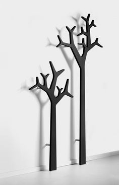 three black trees with no leaves on them in front of a white wall and floor