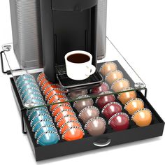 a coffee maker with many different colored balls in front of it and a cup on the tray