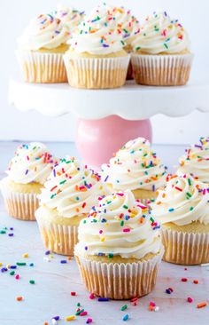 cupcakes with white frosting and sprinkles on a cake stand