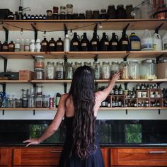 a woman standing in front of a shelf filled with bottles and jars on top of wooden shelves