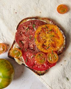 a toasted sandwich with tomatoes, cheese and herbs on it next to a green tomato