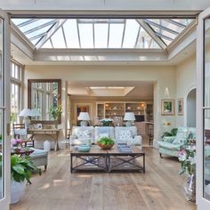 a living room filled with lots of furniture under a glass ceiling covered in light wood flooring