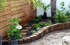 a wooden fence and some plants in the middle of a graveled area with rocks on the ground