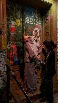 two people standing on the steps in front of a door covered with grafitti