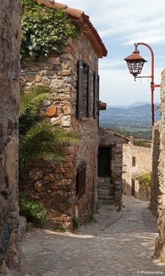 an alley way with stone buildings and plants growing on it