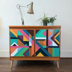 a wooden cabinet with colorful geometric designs painted on the front and sides, next to a lamp