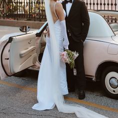 a bride and groom standing in front of a car