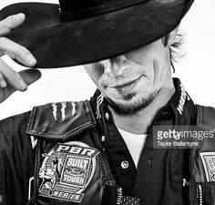 a man wearing a cowboy hat and leather jacket with his hand on the top of his hat