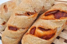 three hot dogs wrapped in bread on a wooden tray next to some other pastries