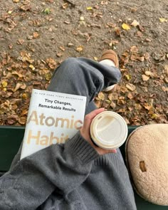 a person sitting on a bench holding a cup of coffee and reading the book atomic haiki