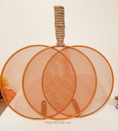 three orange circles with rope hanging from them on a white table next to a vase