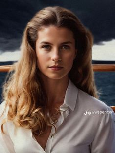 a woman with long blonde hair wearing a white shirt and standing on a boat in the ocean