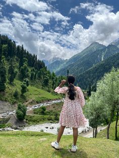 a woman standing on top of a lush green hillside next to a valley filled with trees