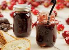 two jars filled with jam next to bread and cherries