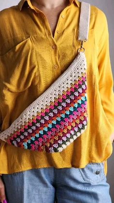 a woman wearing a yellow shirt holding a crocheted purse in her right hand