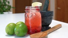 two limes are next to a jar of liquid and a wooden spoon on a table