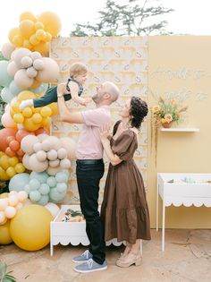 a man and woman standing next to each other in front of a wall with balloons