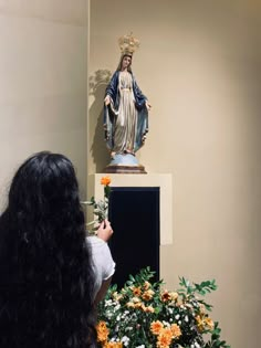 a woman taking a photo of a statue with flowers in the foreground and on the right