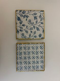 two blue and white tiles with leaves on them are hanging on the wall next to each other