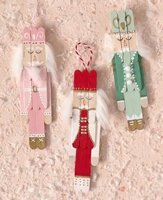 three wooden nutcrackers are hanging on a pink background with white and green feathers