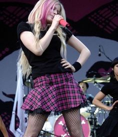 a woman with pink hair and black stockings on singing into a microphone at a concert