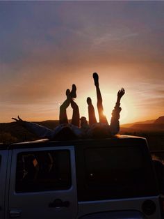 two people laying on the back of a pick up truck with their hands in the air